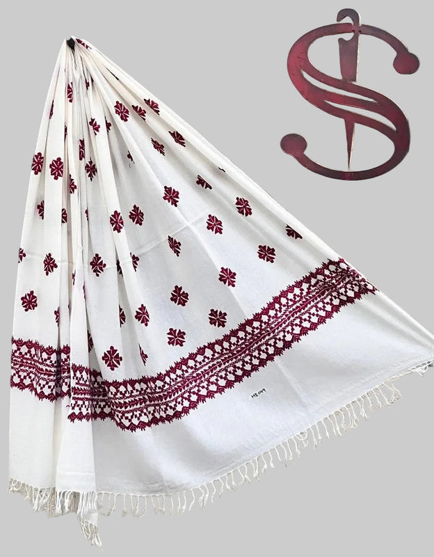 White swati handmade woolen shawl with handmade embroidery draped over a branch of a product display tree in front of a homebased online ecommerce warehouse with a saidaar handmade products logo .swat , kpk , pakistan .
